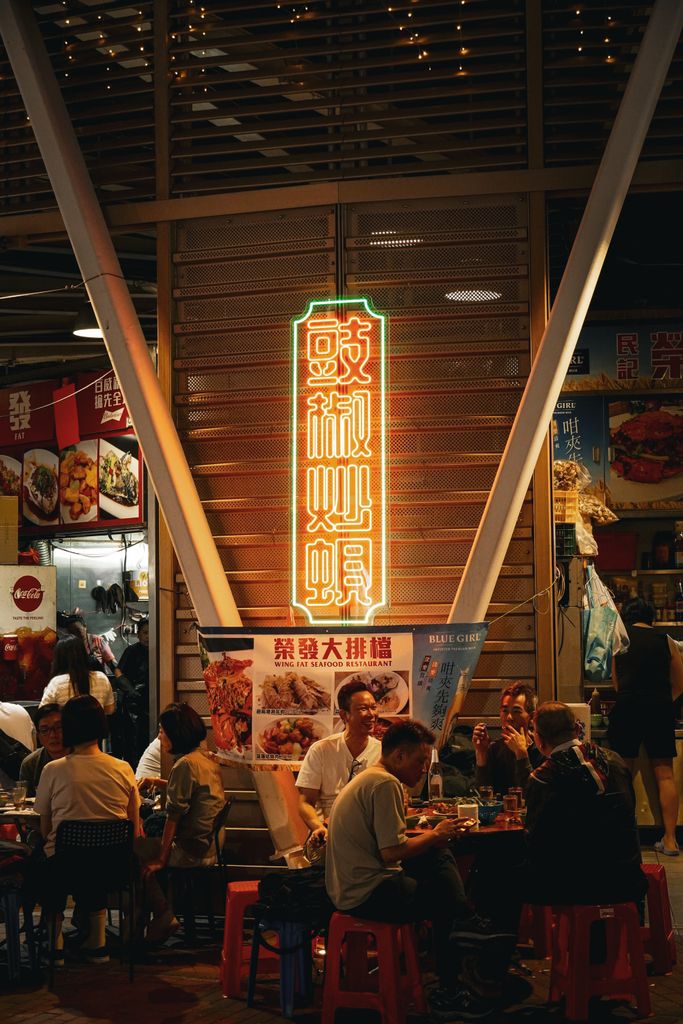 Capture the lively atmosphere of a Hong Kong street market at night with neon signs and dining locals.