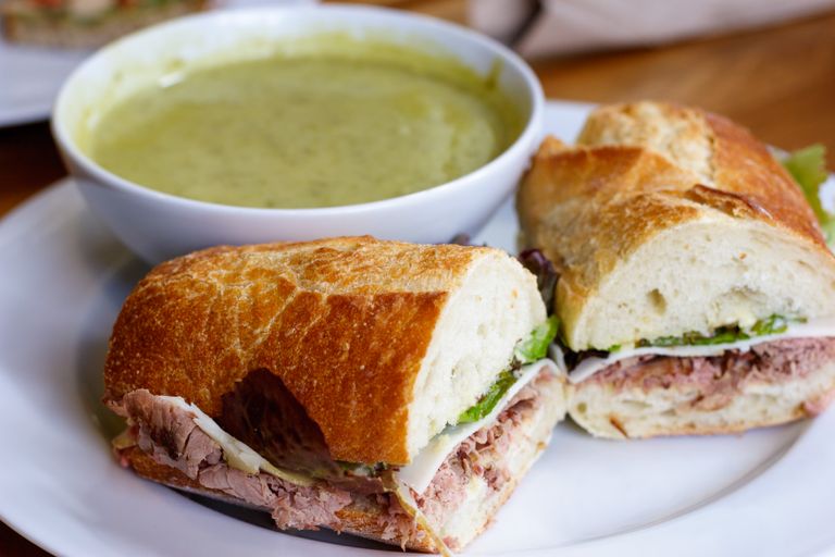Close-up of sandwiches with meat and cheese paired with a bowl of green soup.